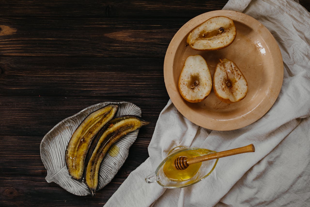 A rustic breakfast setup featuring baked pears, banana slices, and honey on a wooden table.